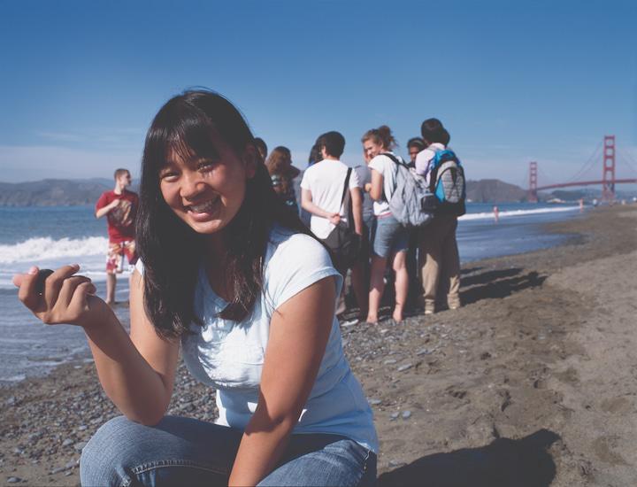 Teenage girl at Baker Beach with Golden Gate Bridge and a group of teenage friends in the background.