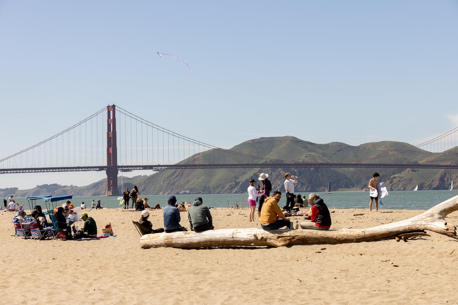 A dozen people sitting at East Beach with the Golden Gate Bridge in the background.